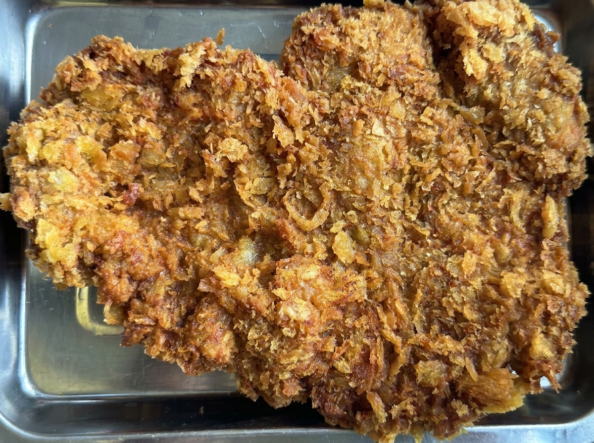 Une côtelette de bœuf frite bien dorée sur un plateau en métal, nappée de sauces au yaourt mentholé et moutarde au miel.
