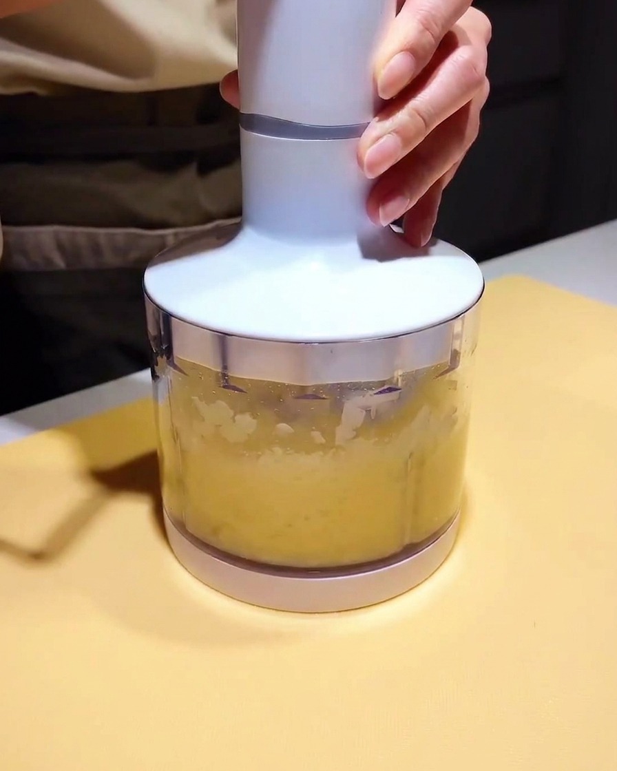 Un petit bol mixeur rempli dune purée claire et dune base de marinade sombre, prêt à être mixé.