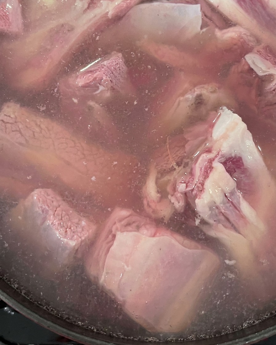 Côtes de bœuf crues et gingembre bouillant dans une casserole deau.