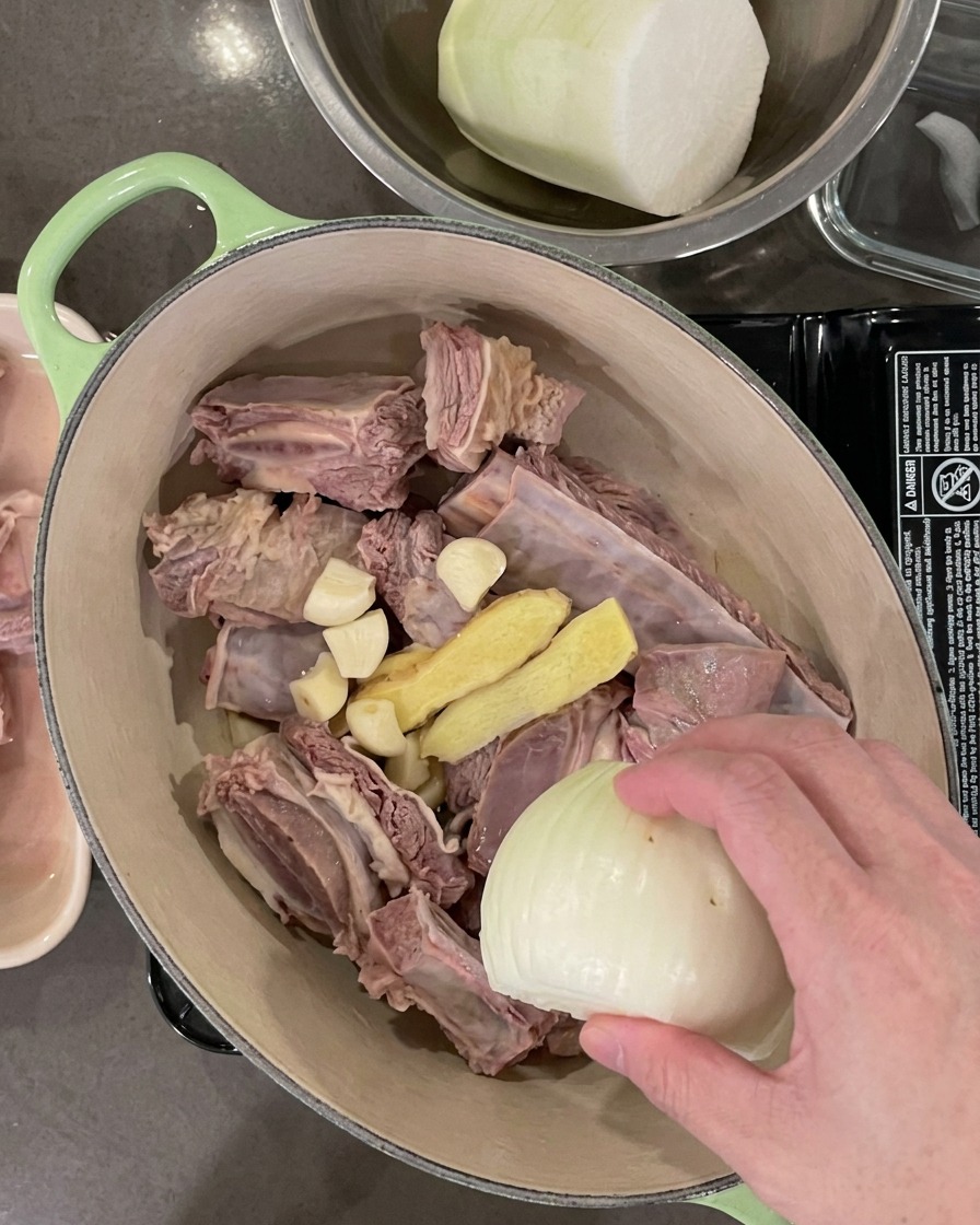 La marmite contenant les côtes inclut maintenant des gousses dail, des tranches de gingembre, un demi-oignon et des oignons verts.