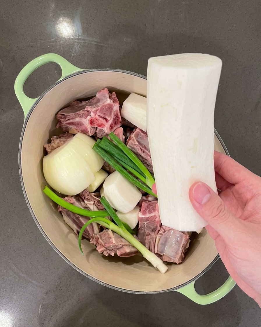 Main plaçant de gros morceaux de radis blanc dans la marmite avec la viande et les aromates.