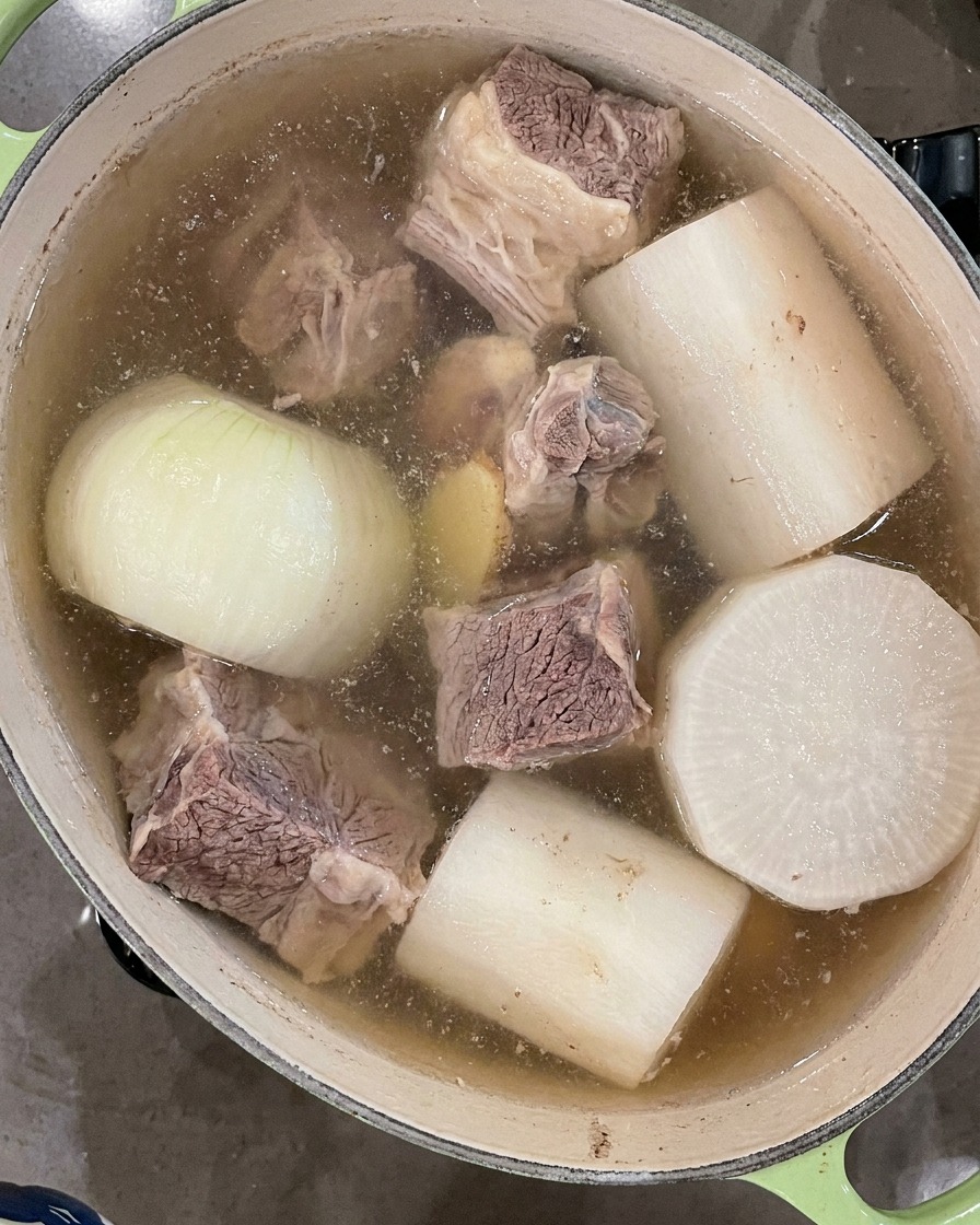 Une louche noire écumant la mousse flottant à la surface de la soupe bouillonnante.