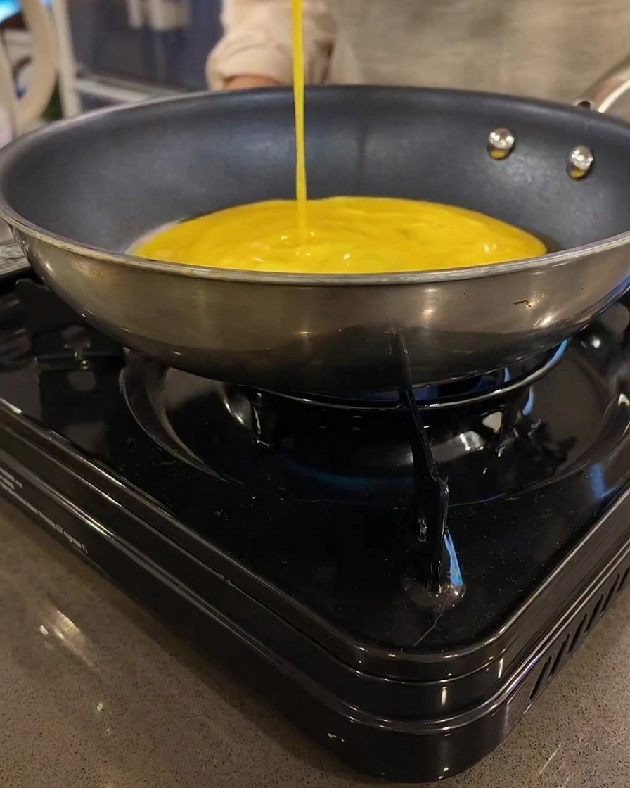 Une fine crêpe aux œufs jaune cuisant dans une poêle plate sur une plaque chauffante.