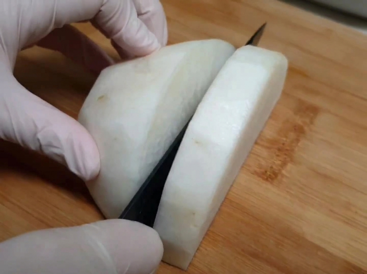 Radis blanc découpé sur une planche en bois par des mains portant des gants de cuisine.