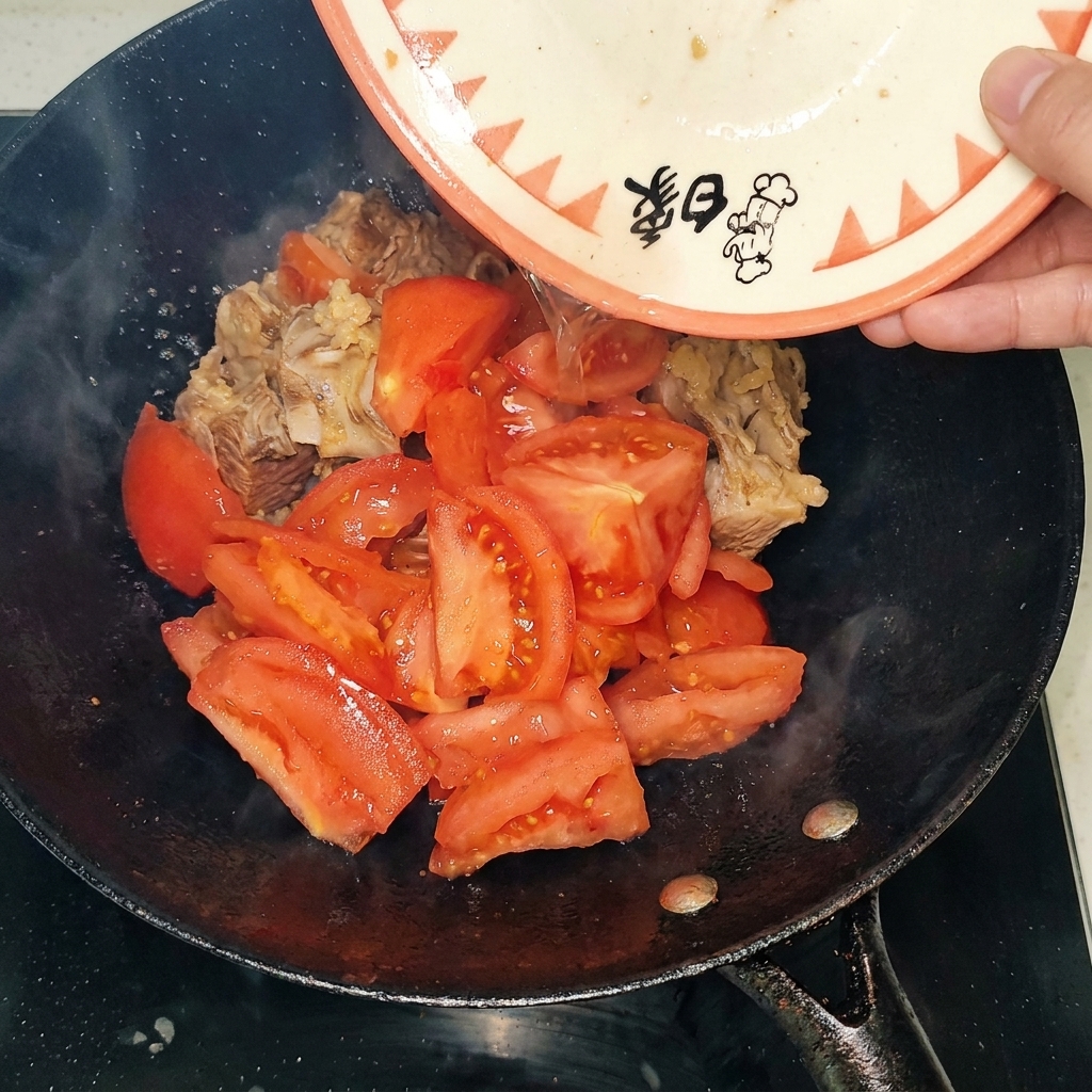 Morceaux de tomates pelées ajoutés au wok avec les travers de bœuf saisis.