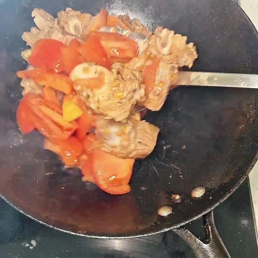 Gros plan sur les travers de bœuf et les tomates sautant dans le wok, montrant le liquide commençant à se former.