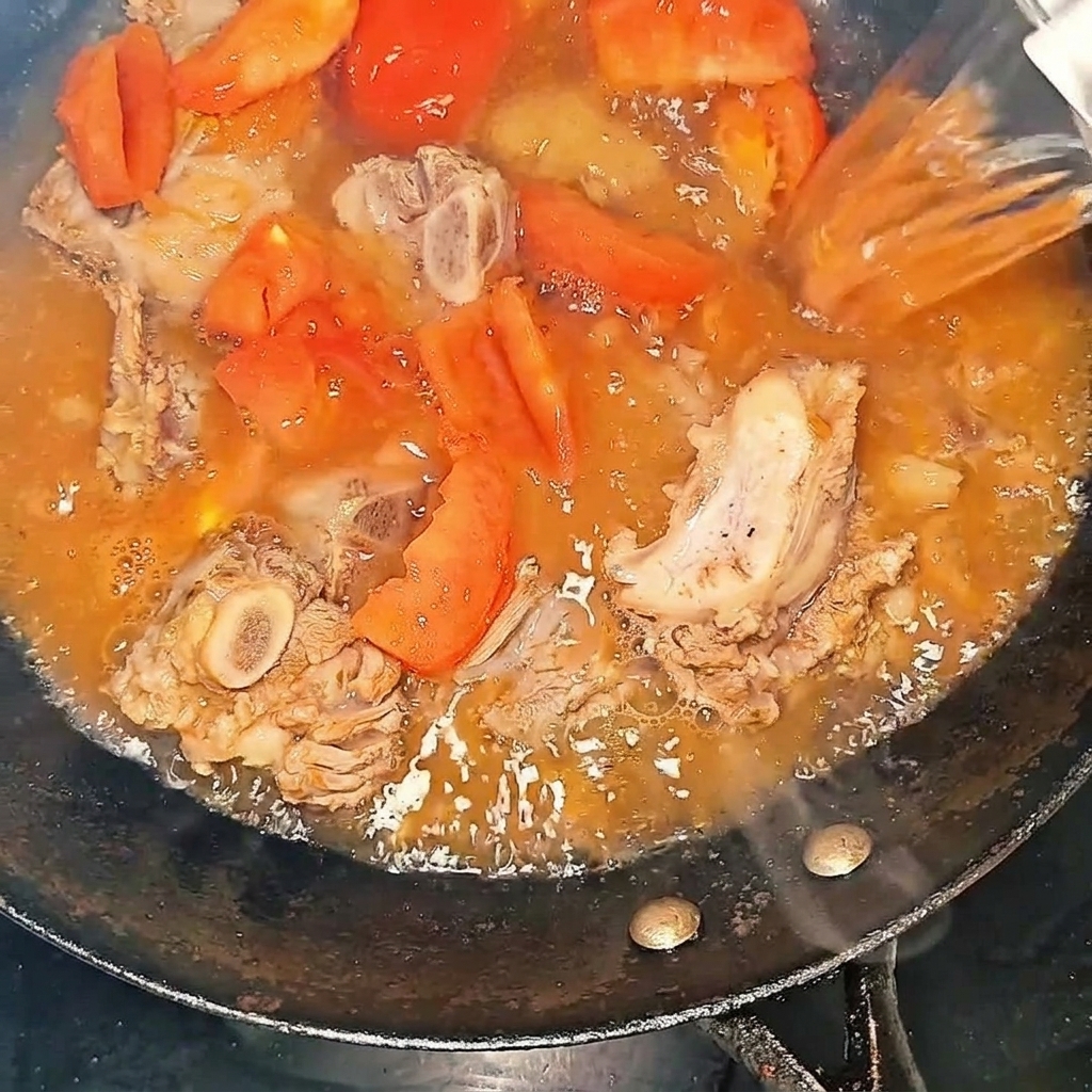 De leau bouillante versée dans le wok avec les travers de bœuf et les tomates.