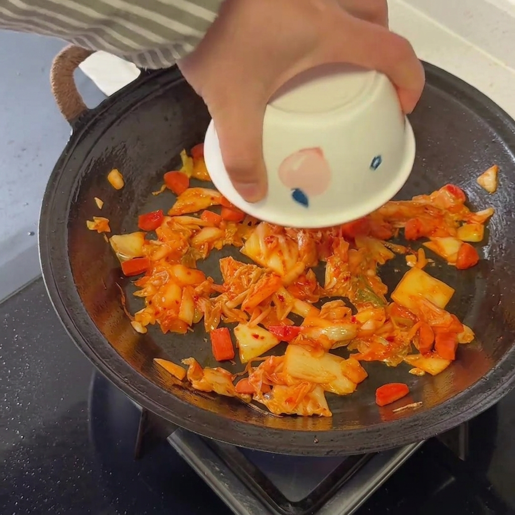 Du riz cuit incorporé soigneusement à la base de kimchi et de saucisse dans une poêle chaude.