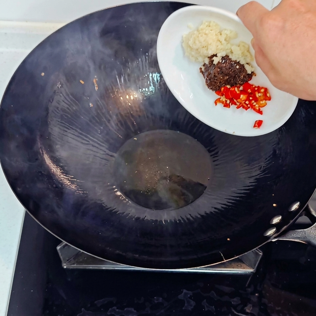 Ajout dail haché, de piment rouge haché et de pâte de soja dans un wok chaud.