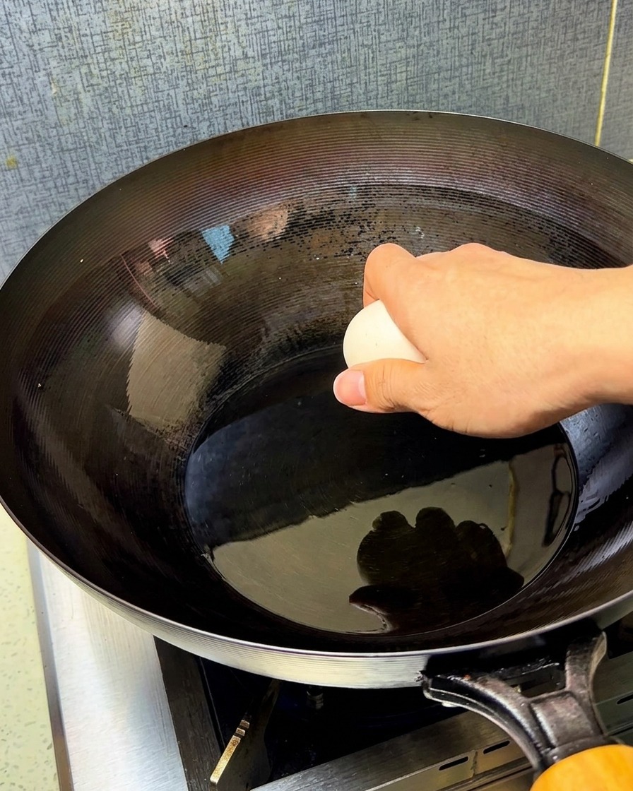 Deux œufs crus tombant dans un wok chaud et huilé.