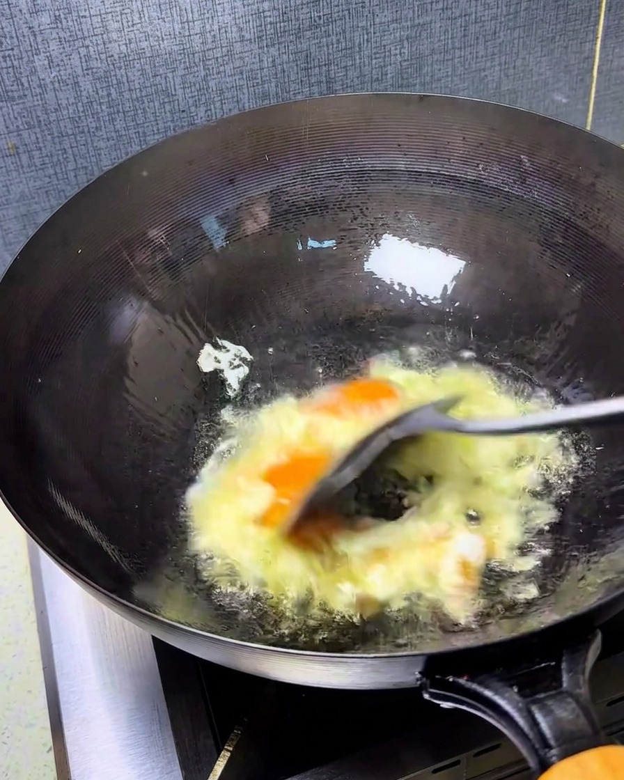 Œufs brouillés rapidement dans un wok chaud avec une spatule, créant des morceaux dorés et moelleux.