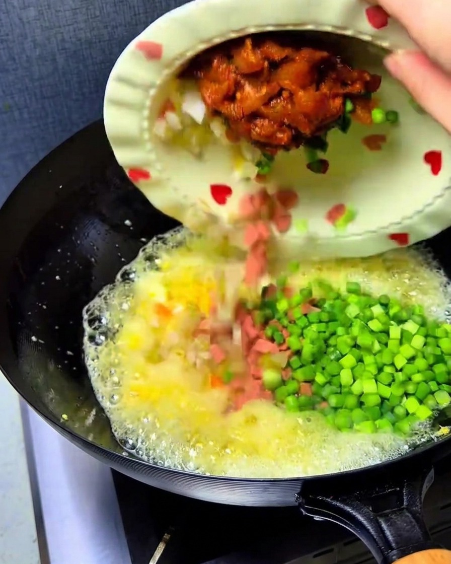 Kimchi haché, dés de jambon, poulet et pousses dail versés dans le wok avec les œufs.