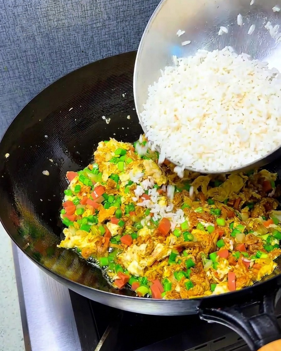 Riz émietté ajouté au wok contenant le mélange dœufs et de légumes.