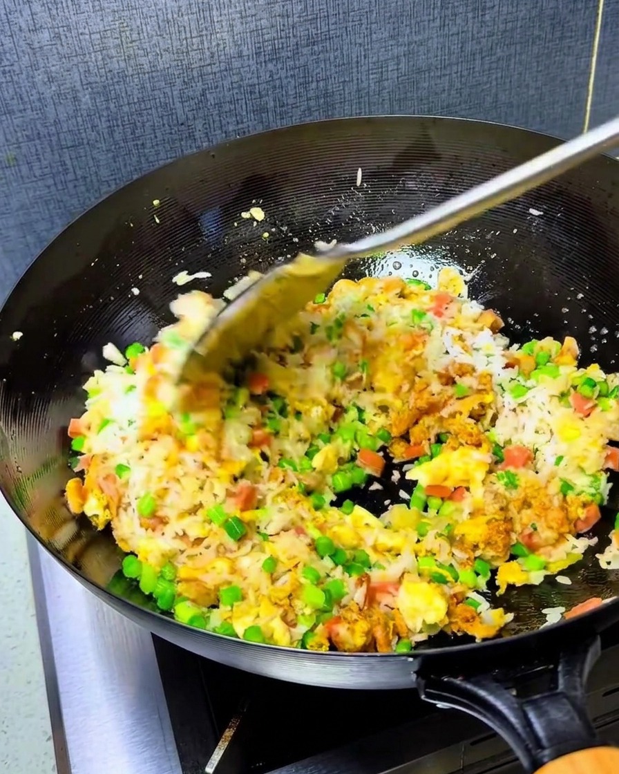 Une cuillère dhuile pimentée rouge vif ajoutée au mélange de riz dans le wok chaud.