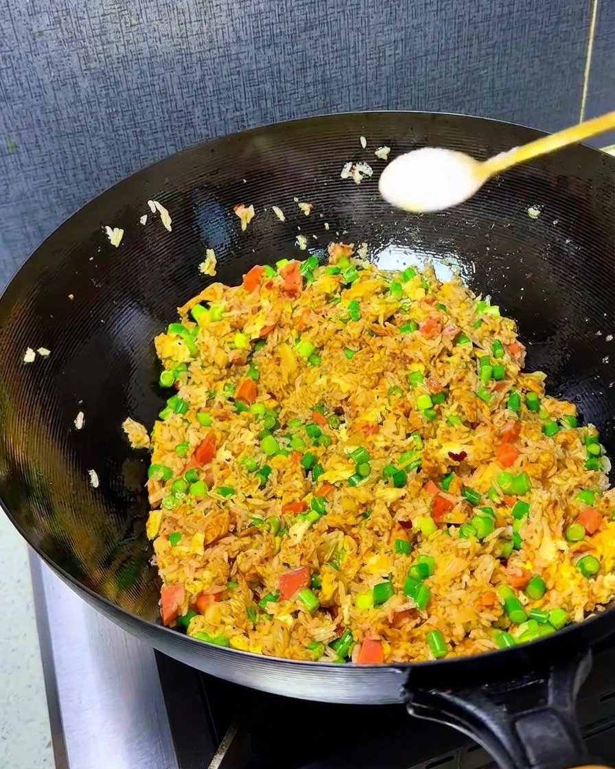 Gros plan de sel et de bouillon de poulet saupoudrés dans un wok rempli de riz sauté coloré.
