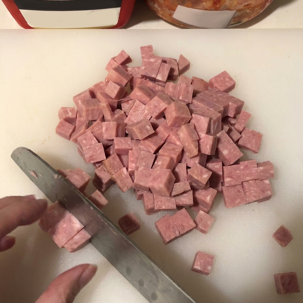 Gros plan sur du spam coupé en petits cubes réguliers sur une surface blanche, avec une lame de couteau visible.