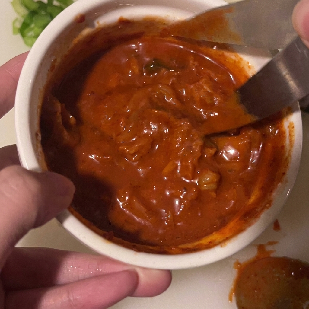 Une paire de ciseaux coupant des morceaux de kimchi directement dans un bol de sauce.
