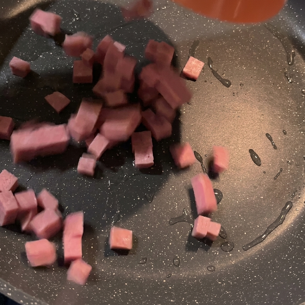 Morceaux de spam en cubes grésillant et dorant dans une poêle chaude.