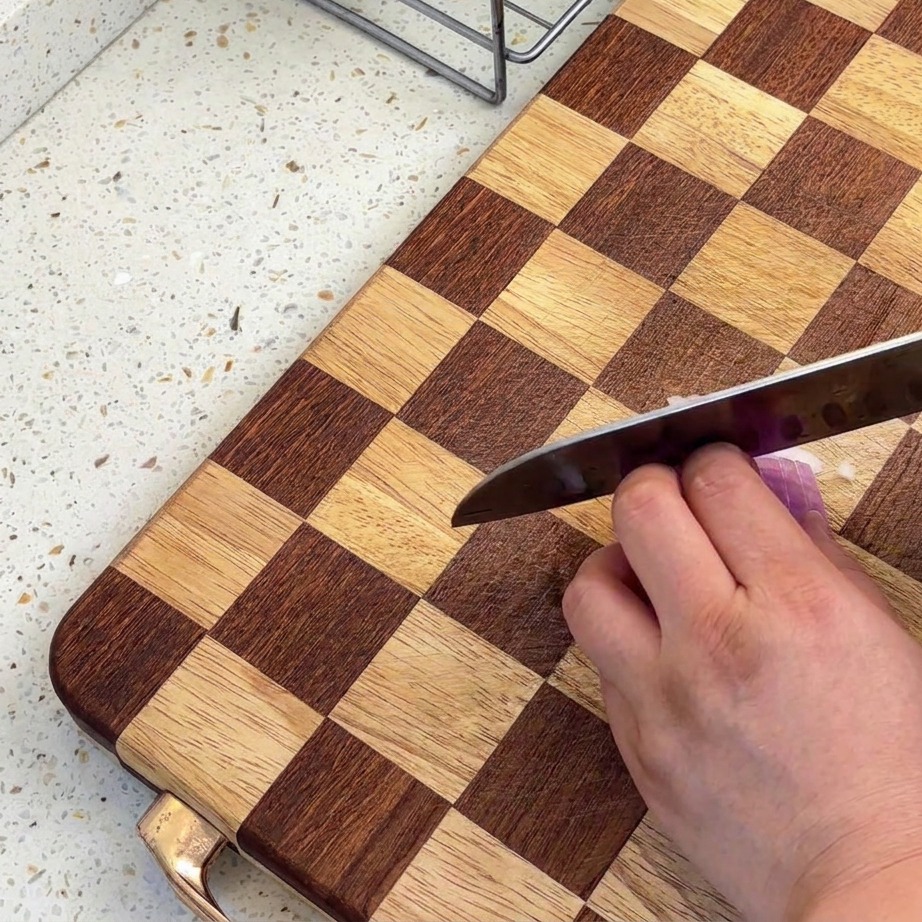 Gros plan sur des échalotes finement hachées sur une planche à découper en bois à carreaux avec un couteau bien aiguisé.