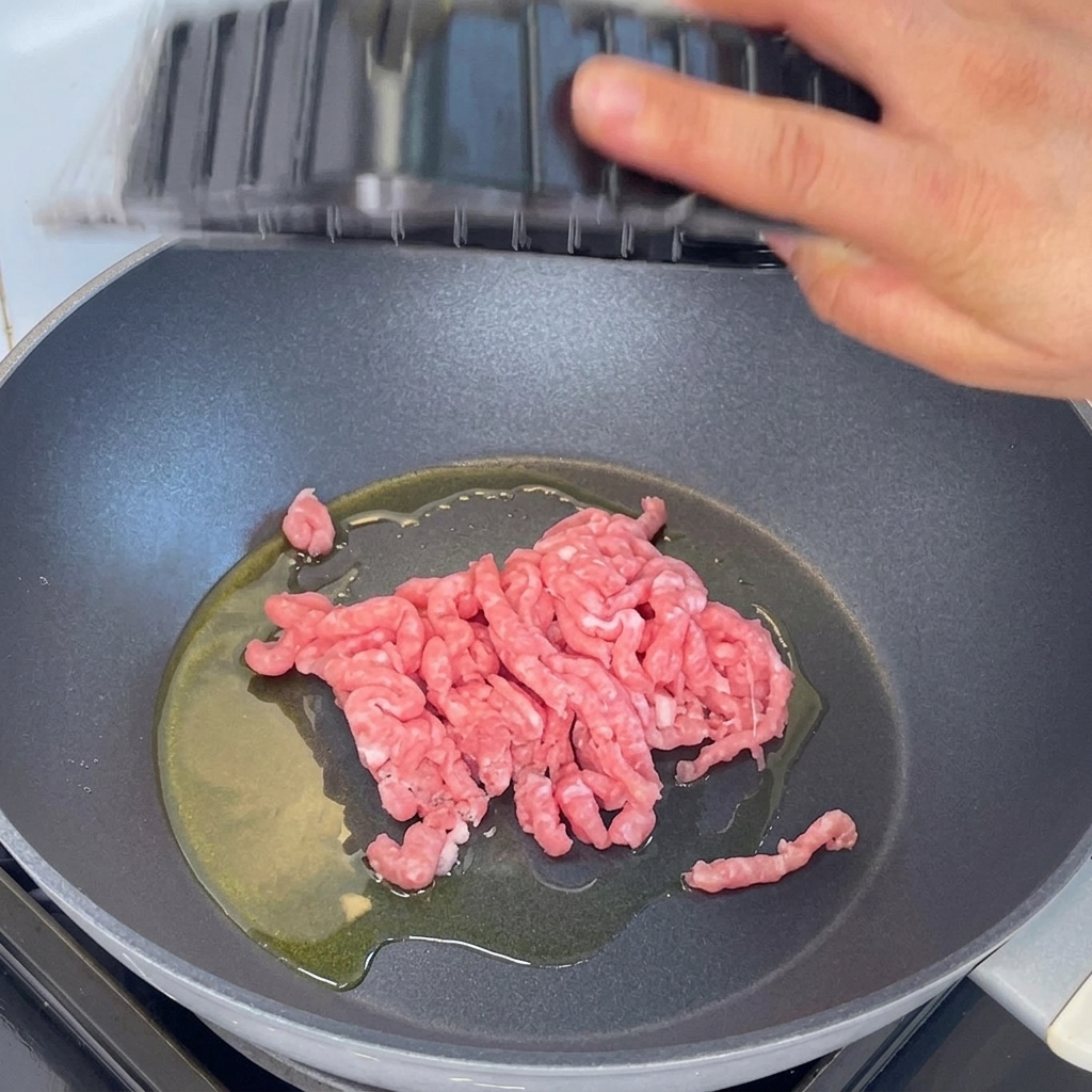 Du porc haché ajouté dans une poêle avec de lhuile chaude et sauté à laide dune spatule en bois.