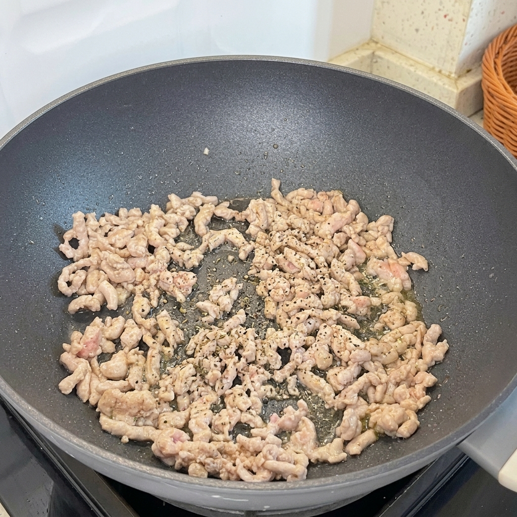 Poivre noir fraîchement moulu ajouté au porc haché en train de dorer dans une poêle.