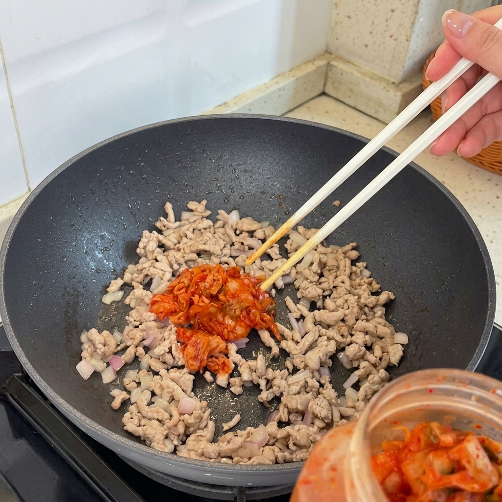 Morceaux de kimchi ajoutés au mélange de viande et déchalotes dans la poêle.