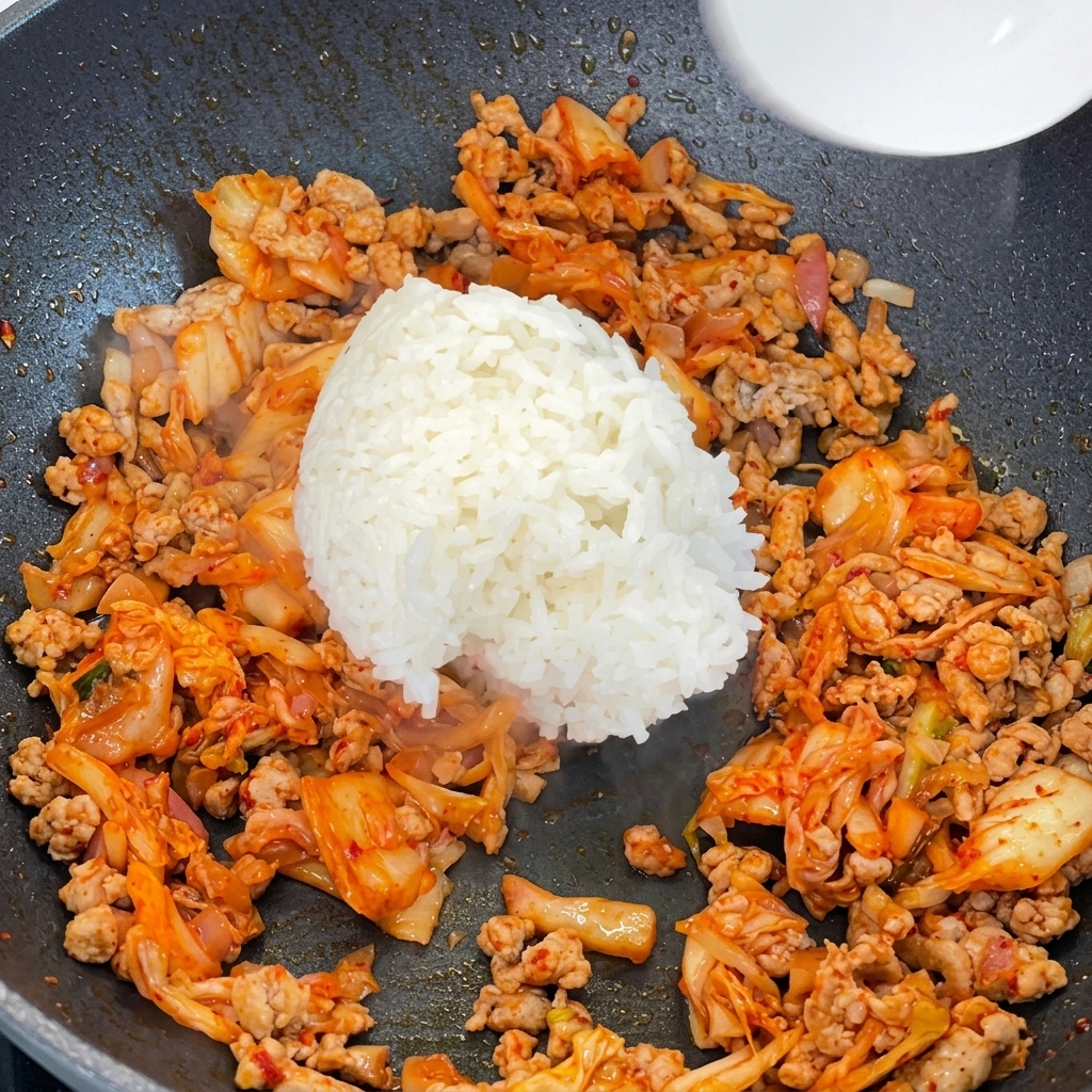 Riz blanc cuit ajouté dans une poêle remplie de porc haché sauté et de kimchi.
