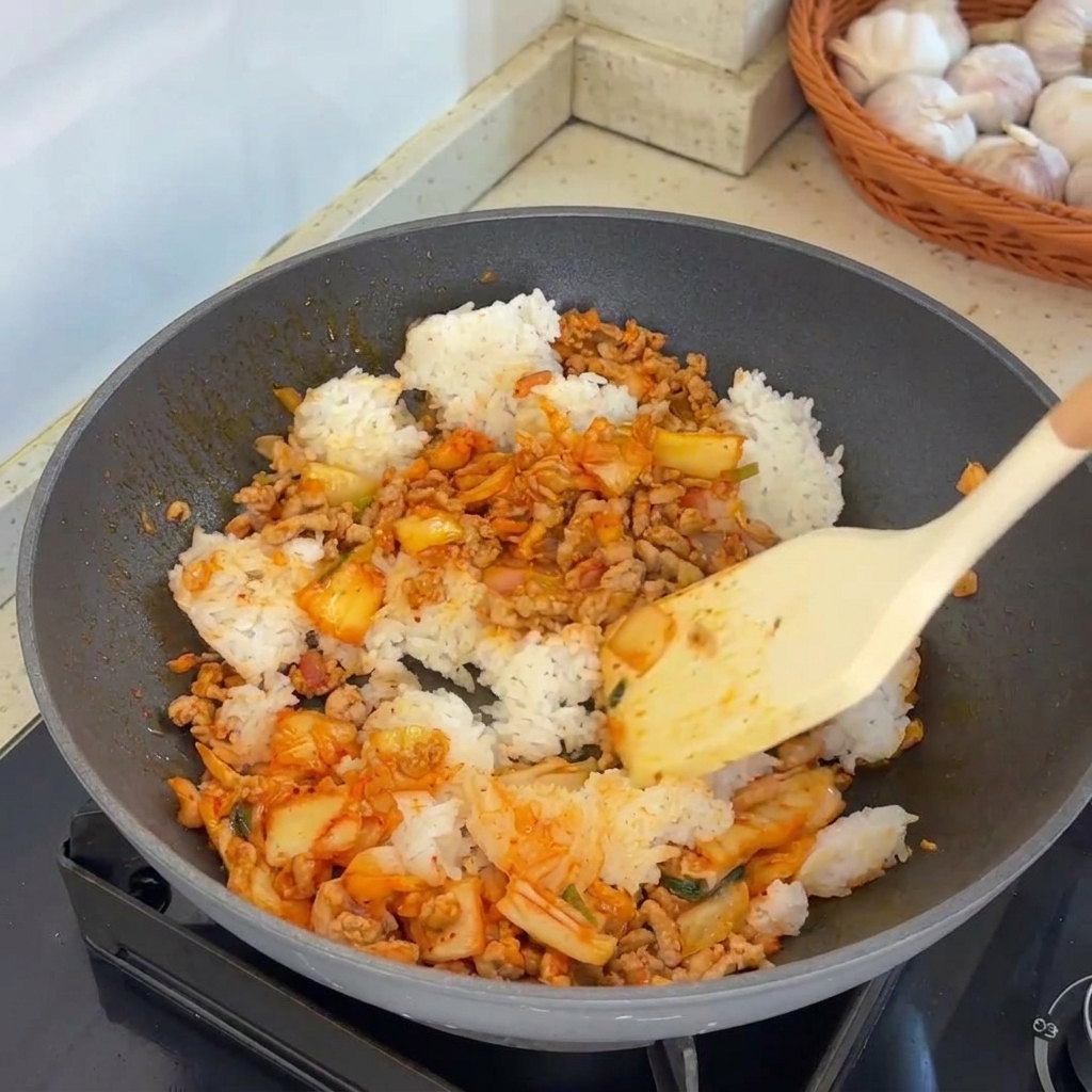 Une spatule remuant vigoureusement le mélange de riz, de viande et de kimchi dans un wok chaud.