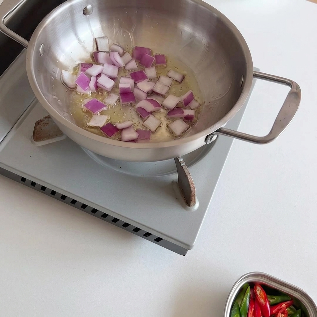 Oignons rouges en dés en train de dorer dans une poêle en inox.