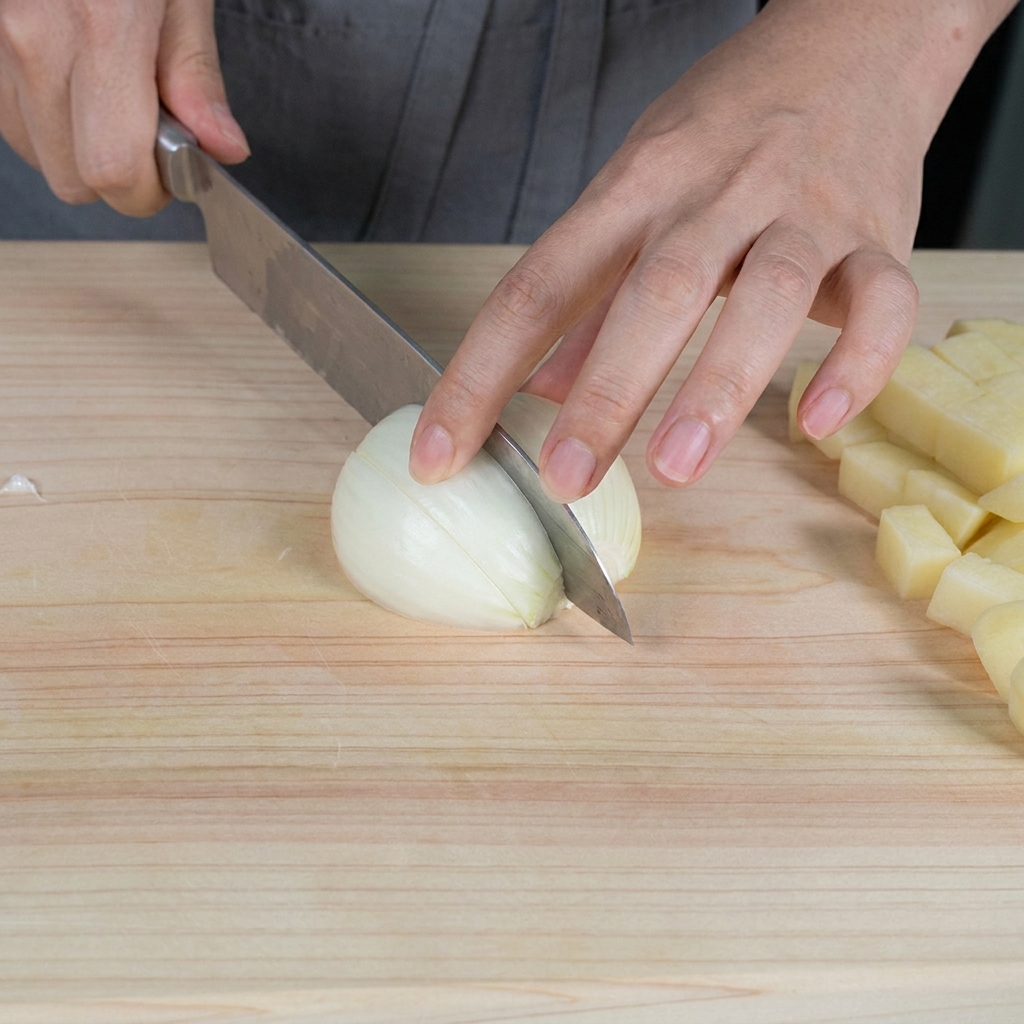 Mains hachant un oignon blanc cru en petits morceaux sur une planche à découper en bois clair.