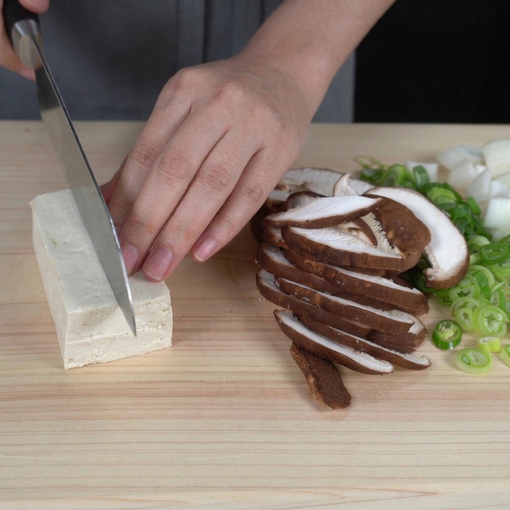 Mains coupant un bloc de tofu blanc ferme en cubes réguliers de la taille dune bouchée sur une planche à découper.