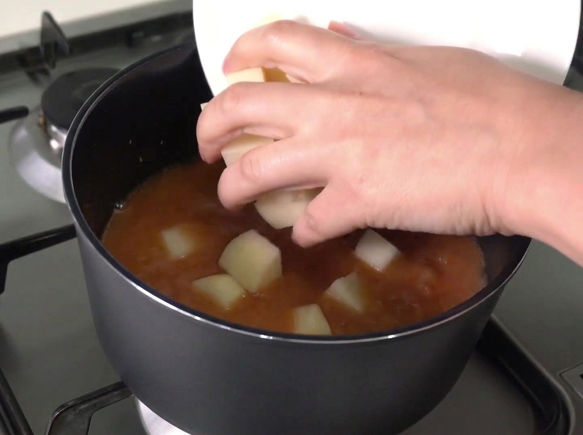 Pommes de terre et oignons hachés glissés dune assiette blanche dans une casserole de bouillon rouge bouillonnant.