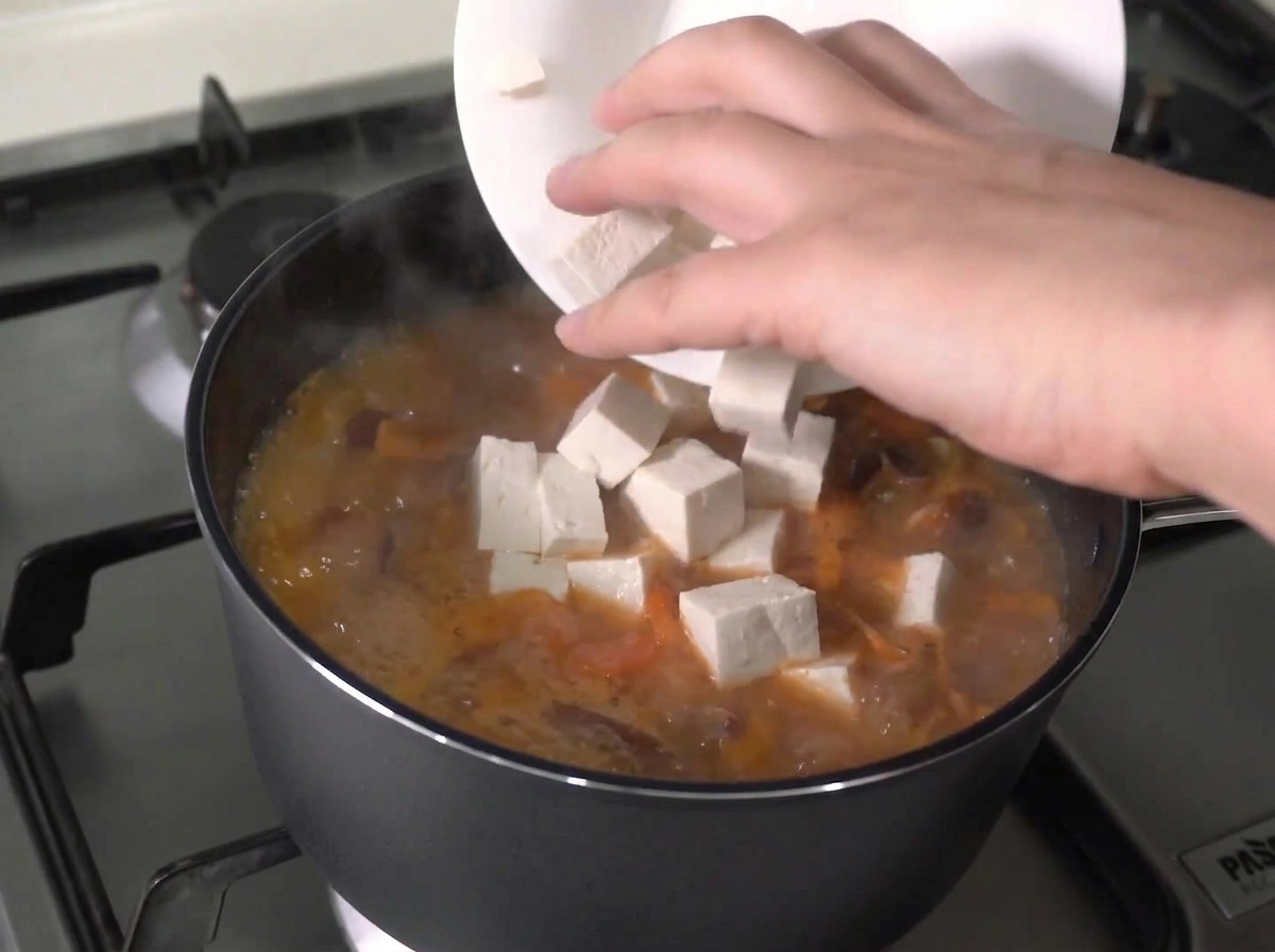 Cubes de tofu frais ajoutés dune assiette blanche dans un ragoût en ébullition active.