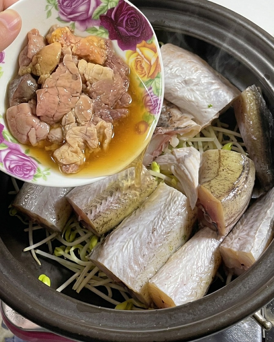 Un petit bol floral versant des œufs de colin frais dans une cocotte contenant déjà le poisson et les pousses de soja.