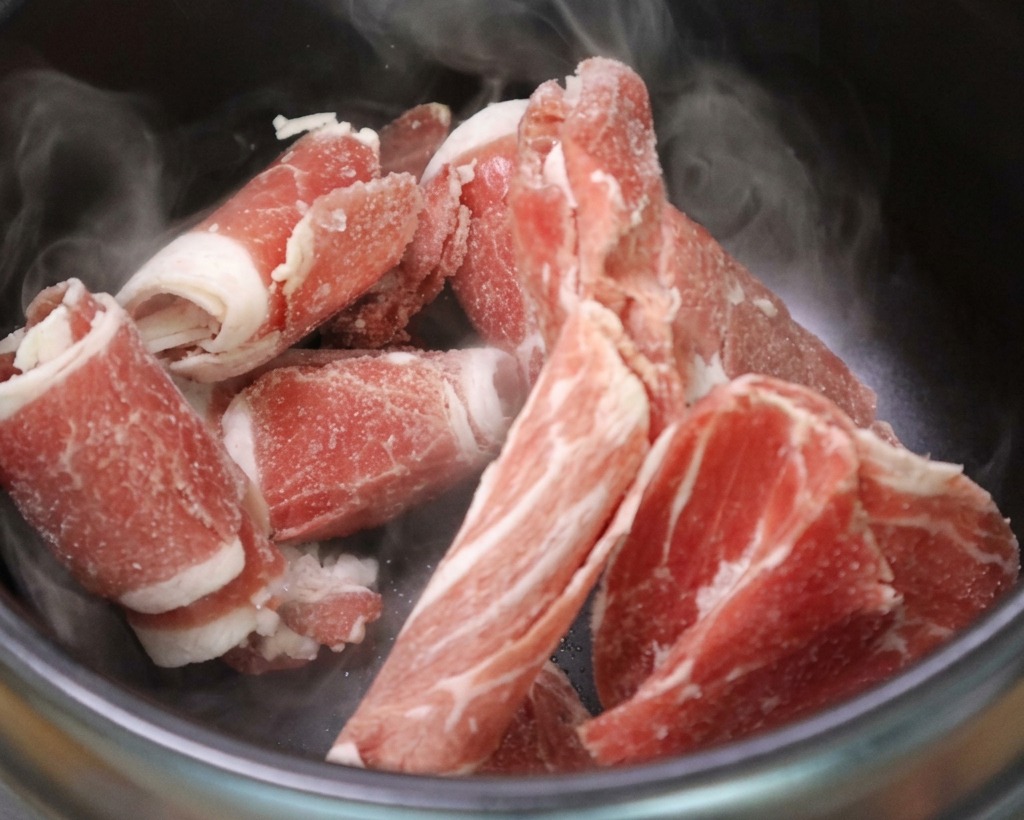 Tranches fines de bœuf grésillant dans un pot en pierre chaud, libérant leur gras.