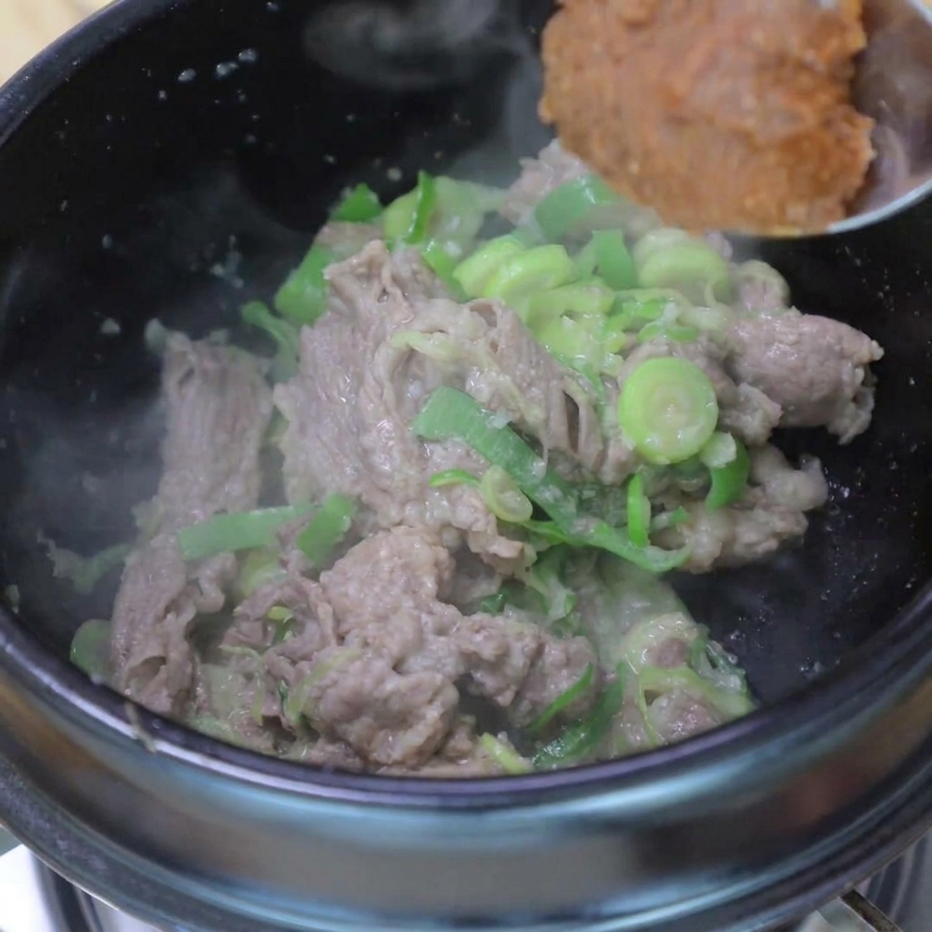 Une cuillerée de pâte de soja ajoutée dans le pot contenant le bœuf et les aromates.