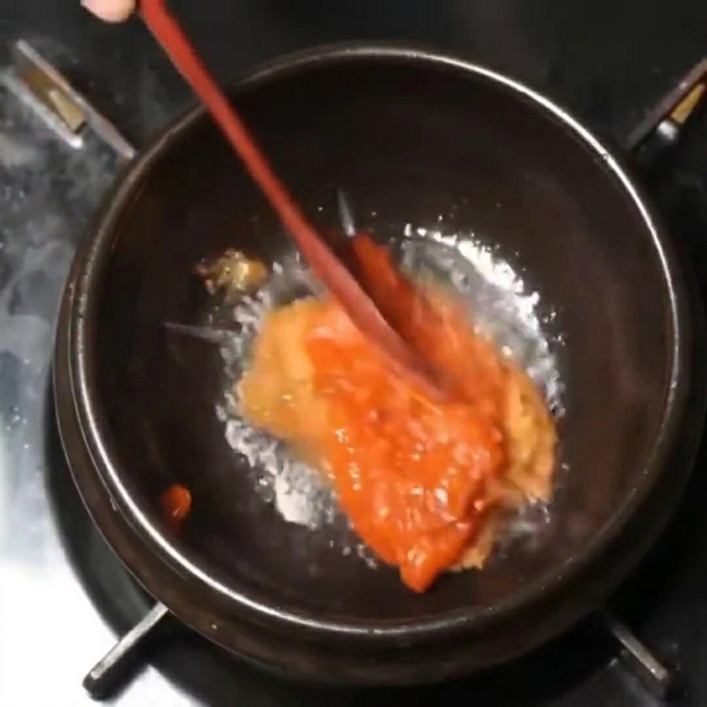 Mélange de pâtes épaisses rouge et marron remué avec une cuillère en bois dans une casserole noire à feu doux.