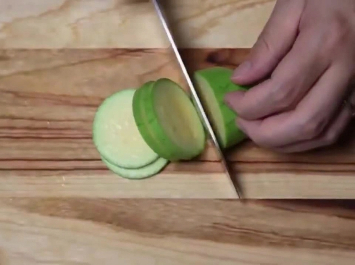 Une courgette verte tranchée en demi-cercles réguliers sur une planche à découper en bois.