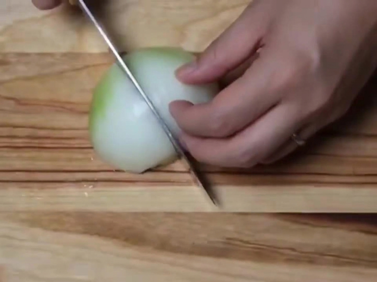 Un oignon blanc coupé en petits morceaux sur une planche en bois.