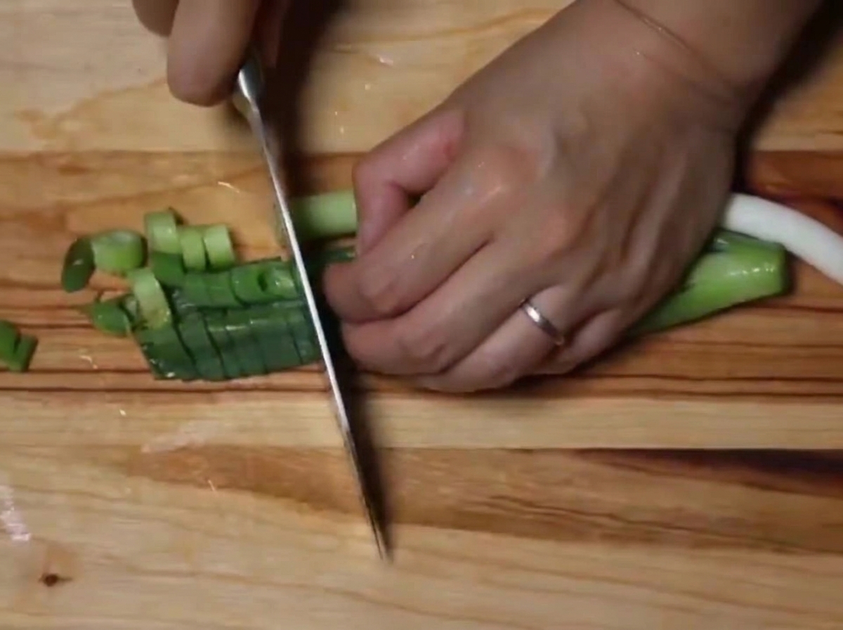 Gros plan sur des oignons verts frais finement coupés en rondelles sur une planche en bois.