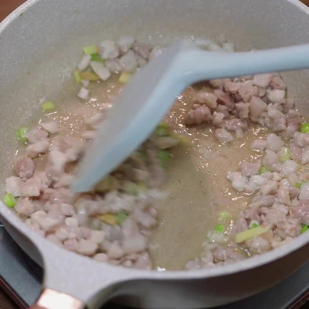 Porc haché en train de revenir dans une poêle avec de la ciboule et du gingembre.