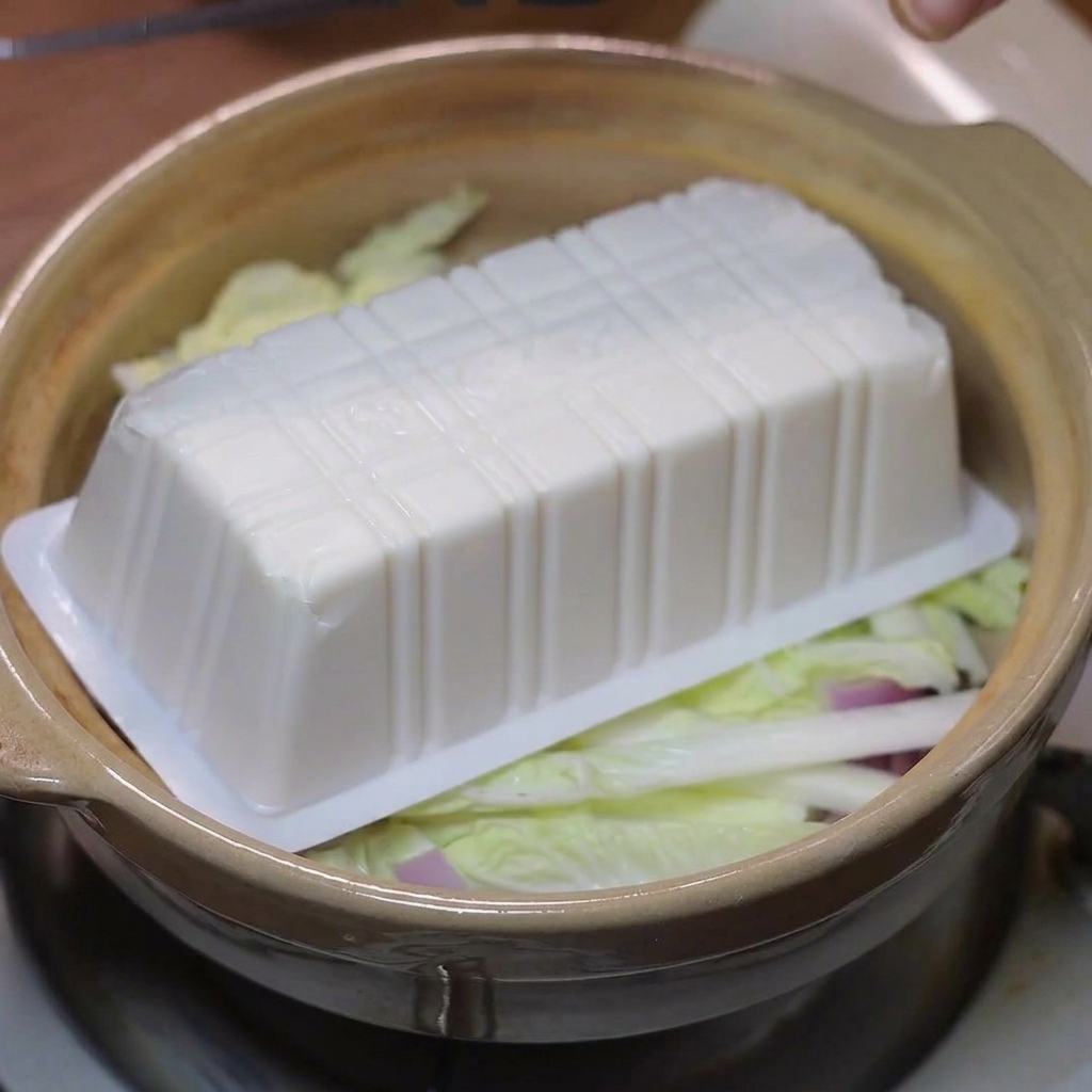 Tranches de tofu soyeux disposées sur le chou et les oignons dans la cocotte.