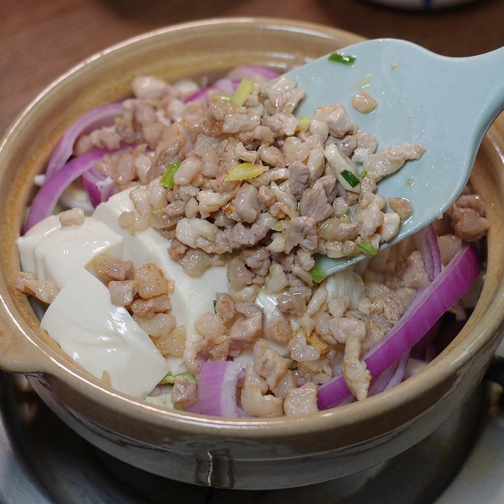 Le porc sauté et la sauce préparée versés sur le tofu dans la cocotte.