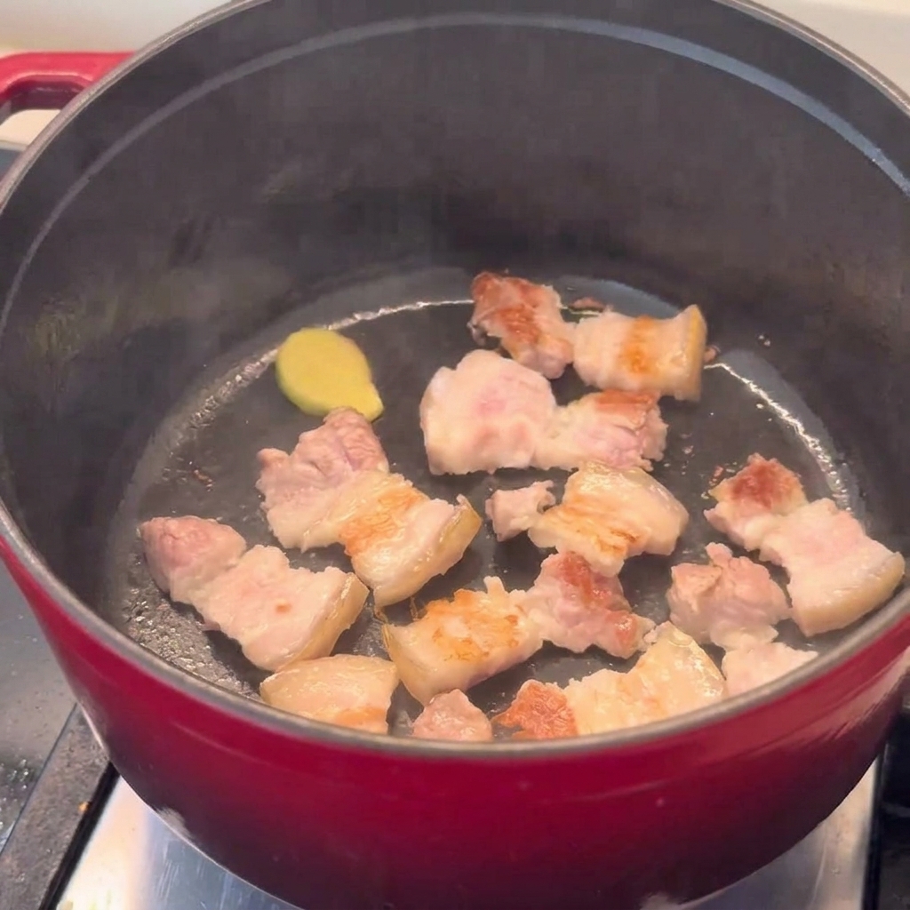 Des morceaux de poitrine de porc dorés sautés dans une marmite rouge.