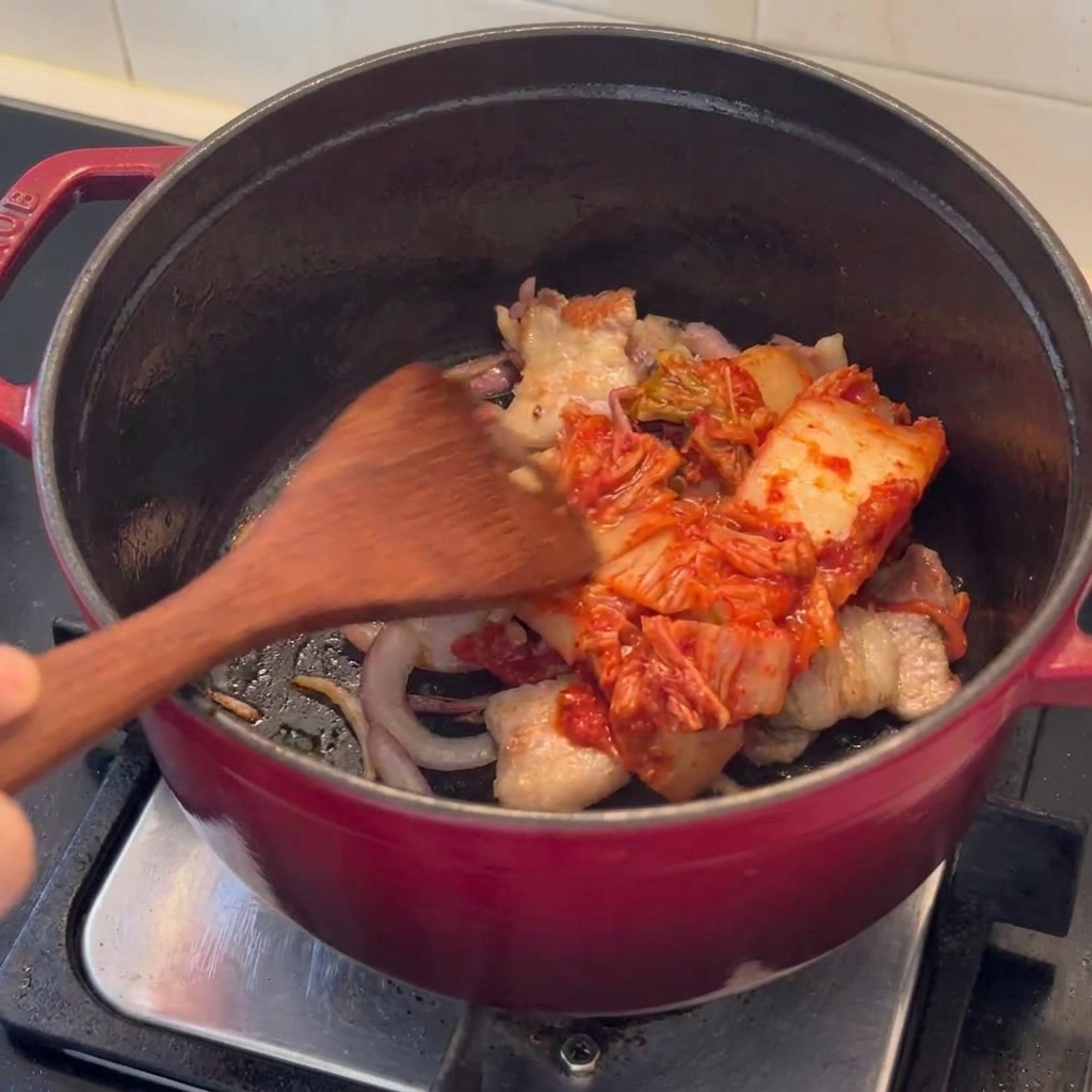 Des morceaux de kimchi sautés avec de la poitrine de porc saisie dans une marmite.