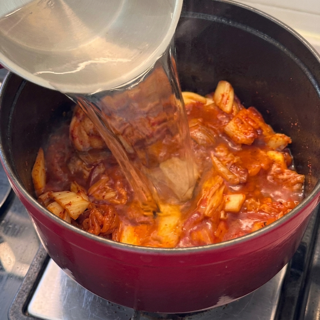 De leau est versée dans la marmite contenant le porc et le kimchi, formant la base du ragoût.