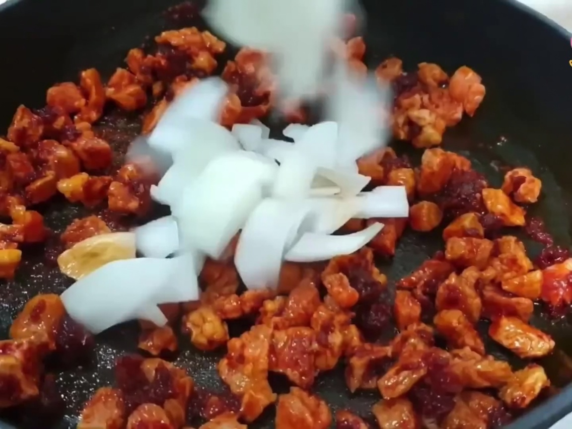 Des dés doignon, de la ciboule et de lail ajoutés à la poêle avec le porc en cours de cuisson.