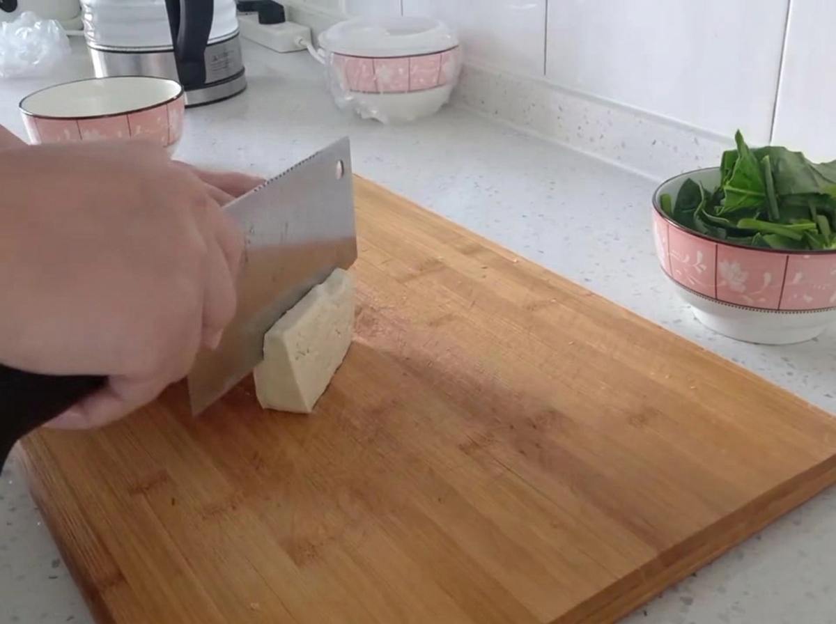 Bloc de tofu ferme coupé en fines lamelles régulières sur une planche en bois.