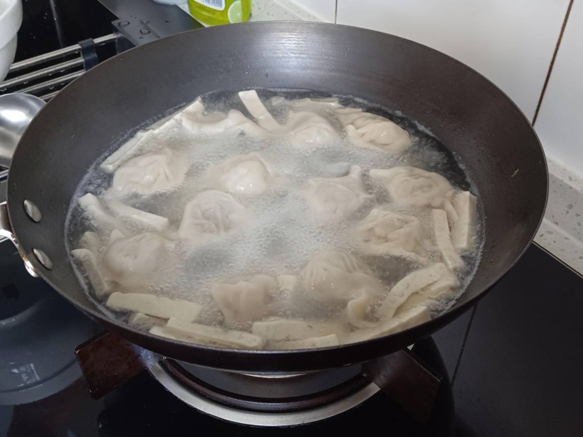 Gros plan de nouilles vermicelles plongées dans la casserole bouillante avec les raviolis et le tofu.