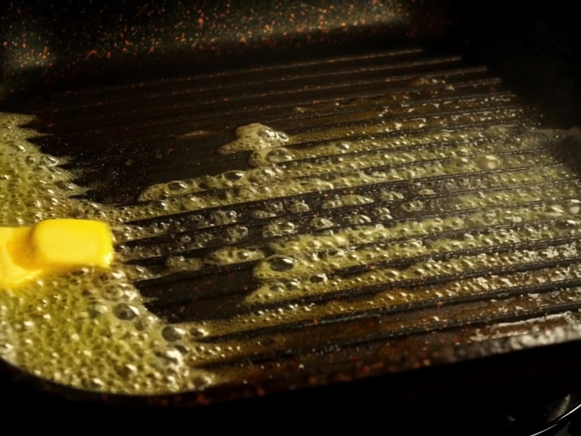 Moitiés de pain à burger toastées dans une poêle grill avec du beurre fondu.